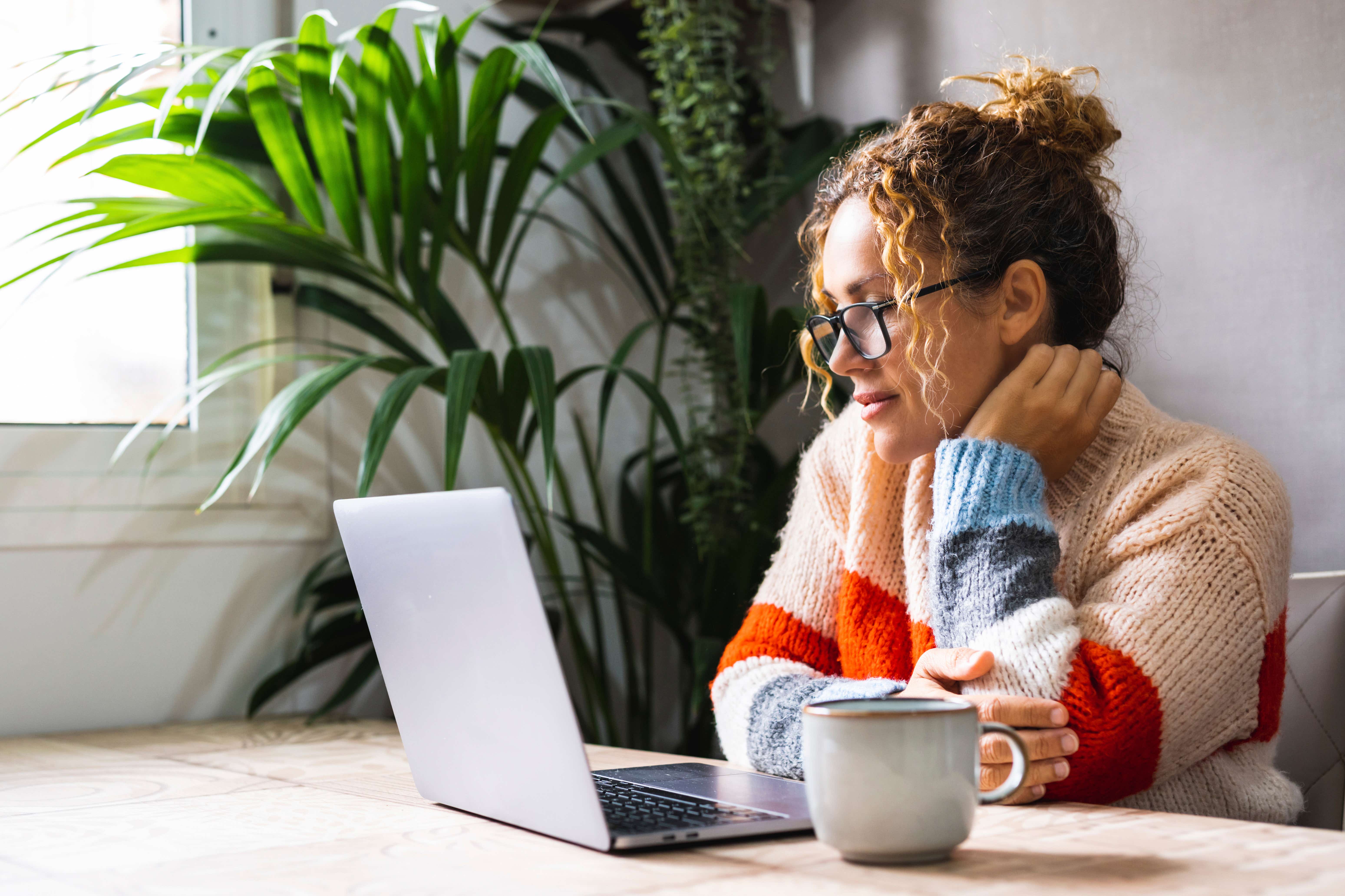 Woman looks at her laptop screen, a cup of coffee by her side.