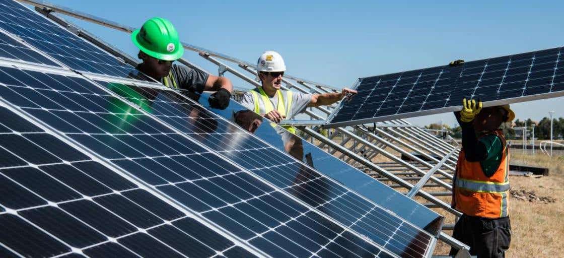 Three construction men working outside in the sun installing solar panels