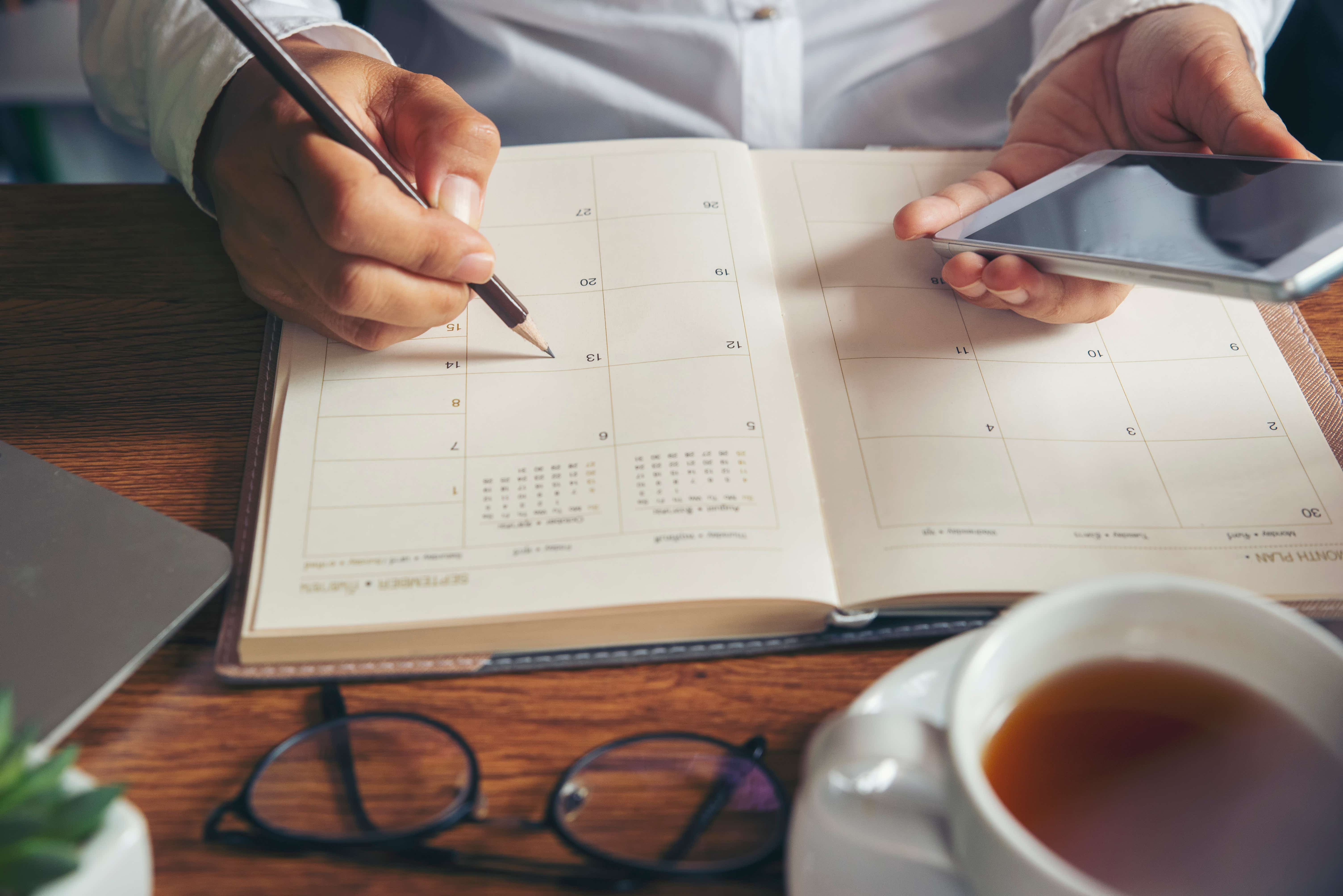 Man holding phone and looking at a calendar on his desk. 