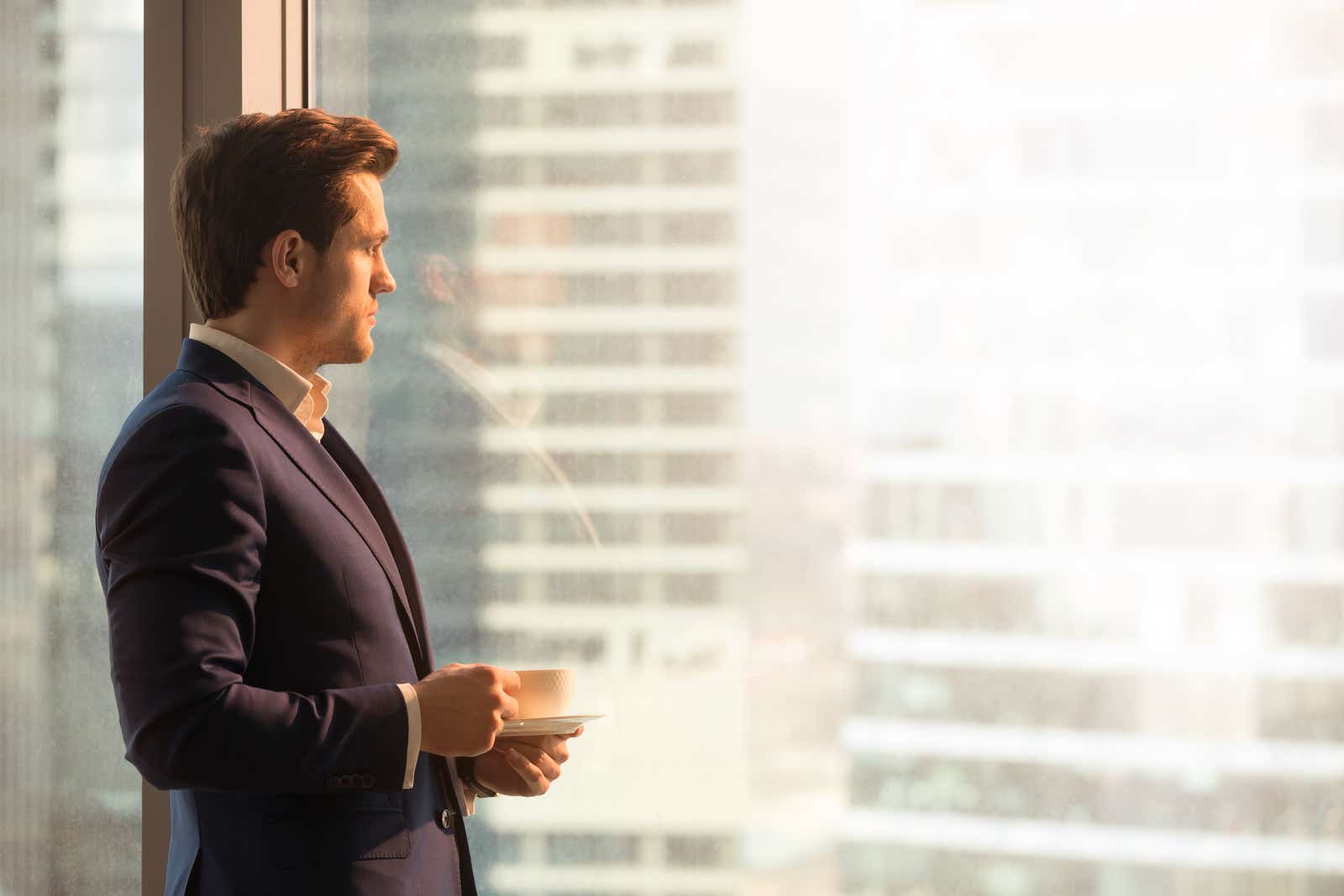 Thoughtful businessman in suit looking through big office window