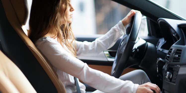 Woman driving a car with one hand on the wheel and the other on the gear stick.