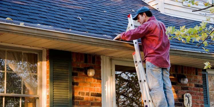 Man on ladder cleaning gutter