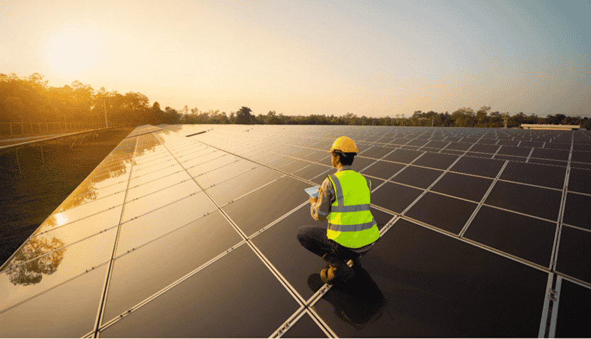 Engineer-wearing-a-safety-vest-and-helmet-inspecting-solar-panels-with-a-tablet-at-a-solar-farm-during-sunset