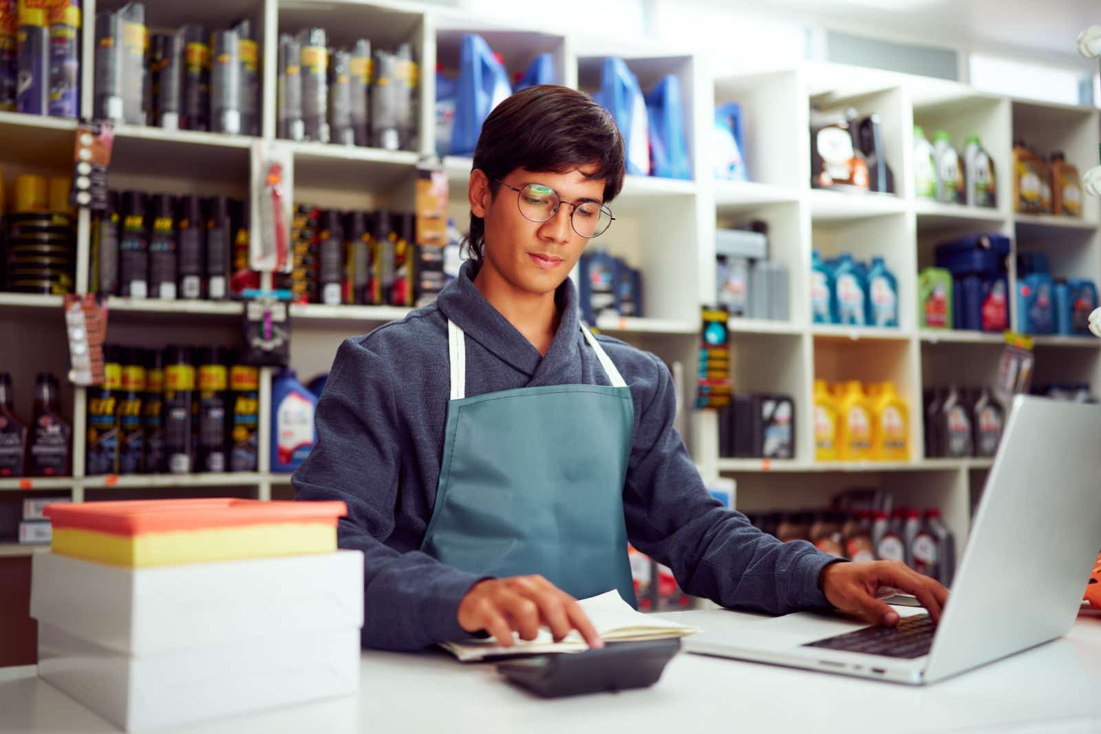 Owner of a car maintenace shop at the counter,  working on his laptop and calculator.