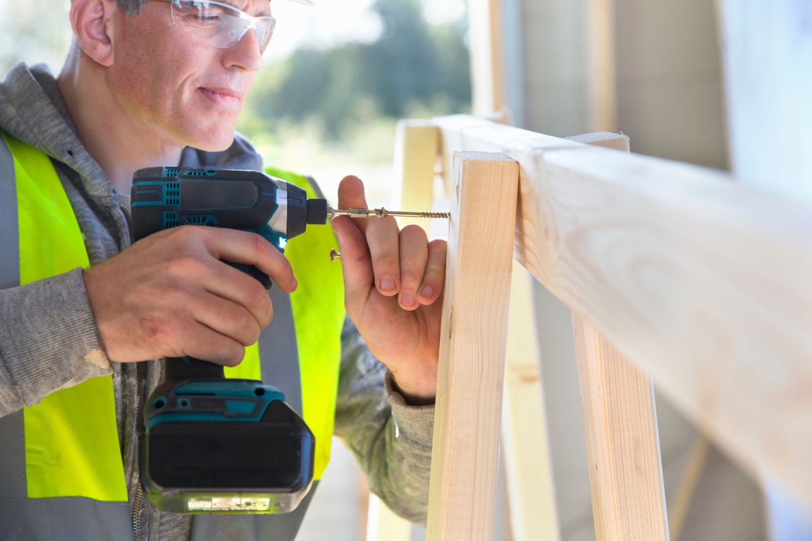 Carpenter in high viz jacket using his power drill.