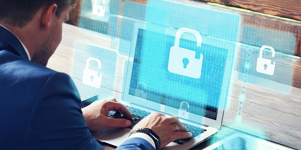 Young businessman working on his laptop in the office, select the icon security on the virtual display.
