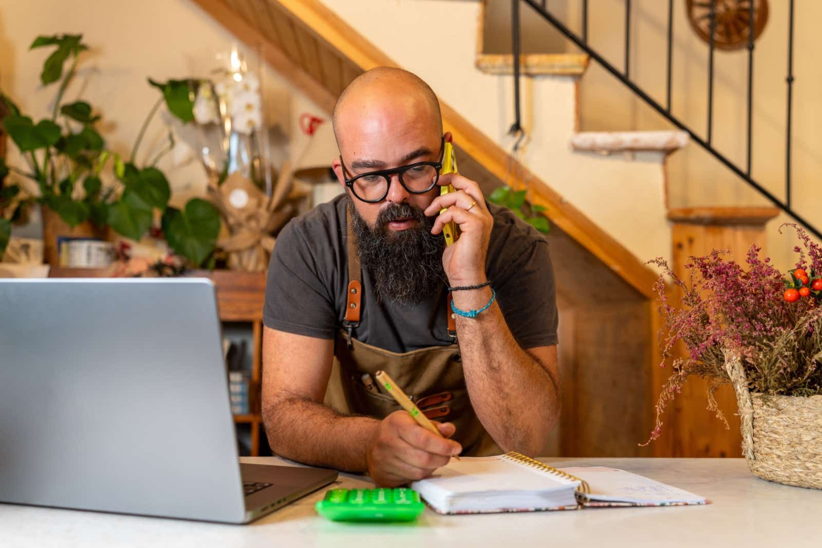 Florist on the phone. In front of him on the counter is his order book, calculator and laptop.