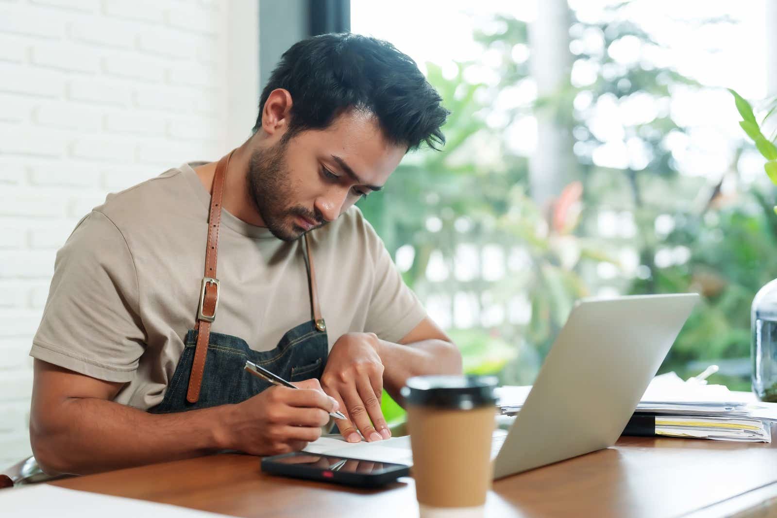 Coffee shop owner sitting at desk, giving serious thought to his company's finances