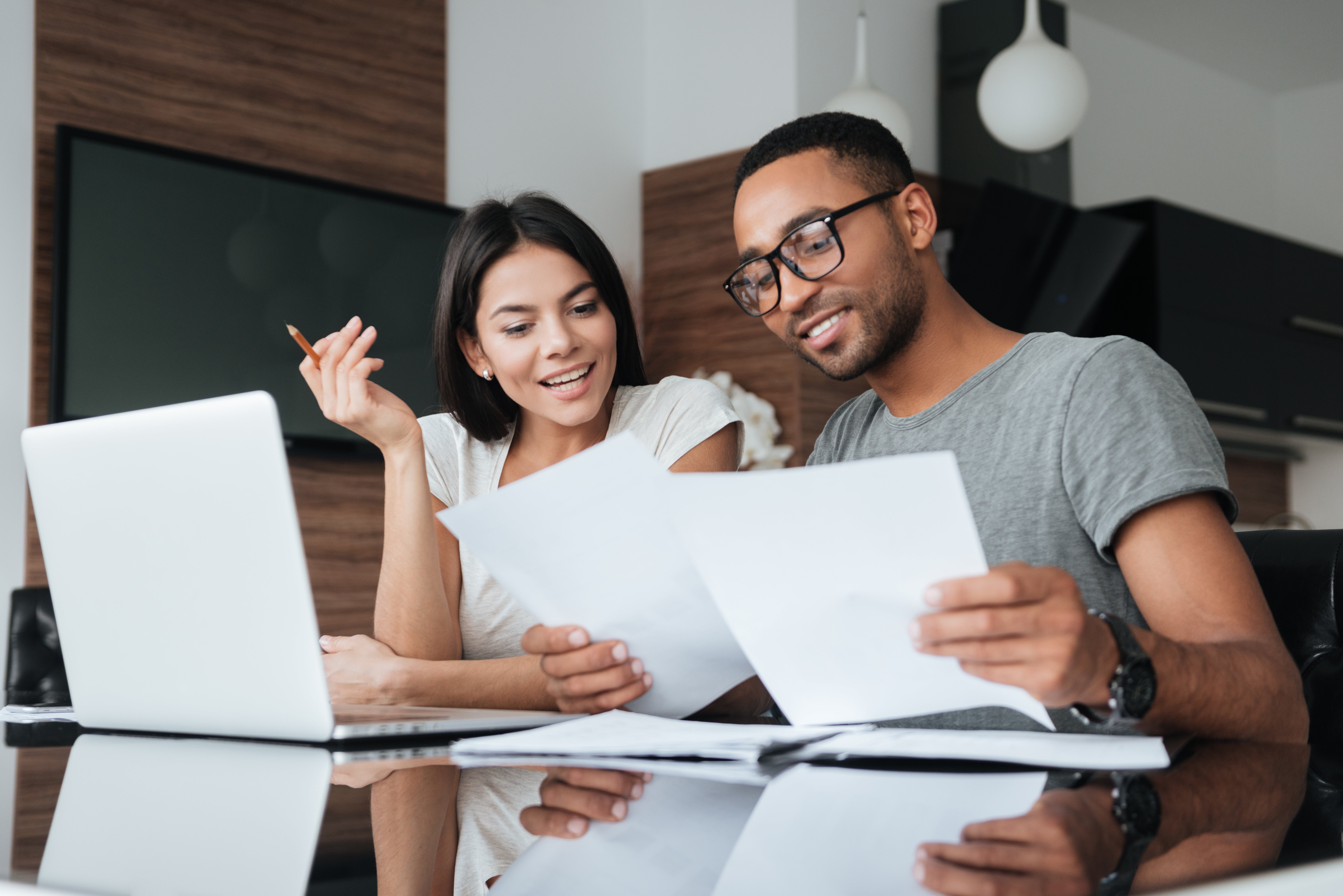 Two people sitting at a desk with a laptop and looking at sheets of paper. 