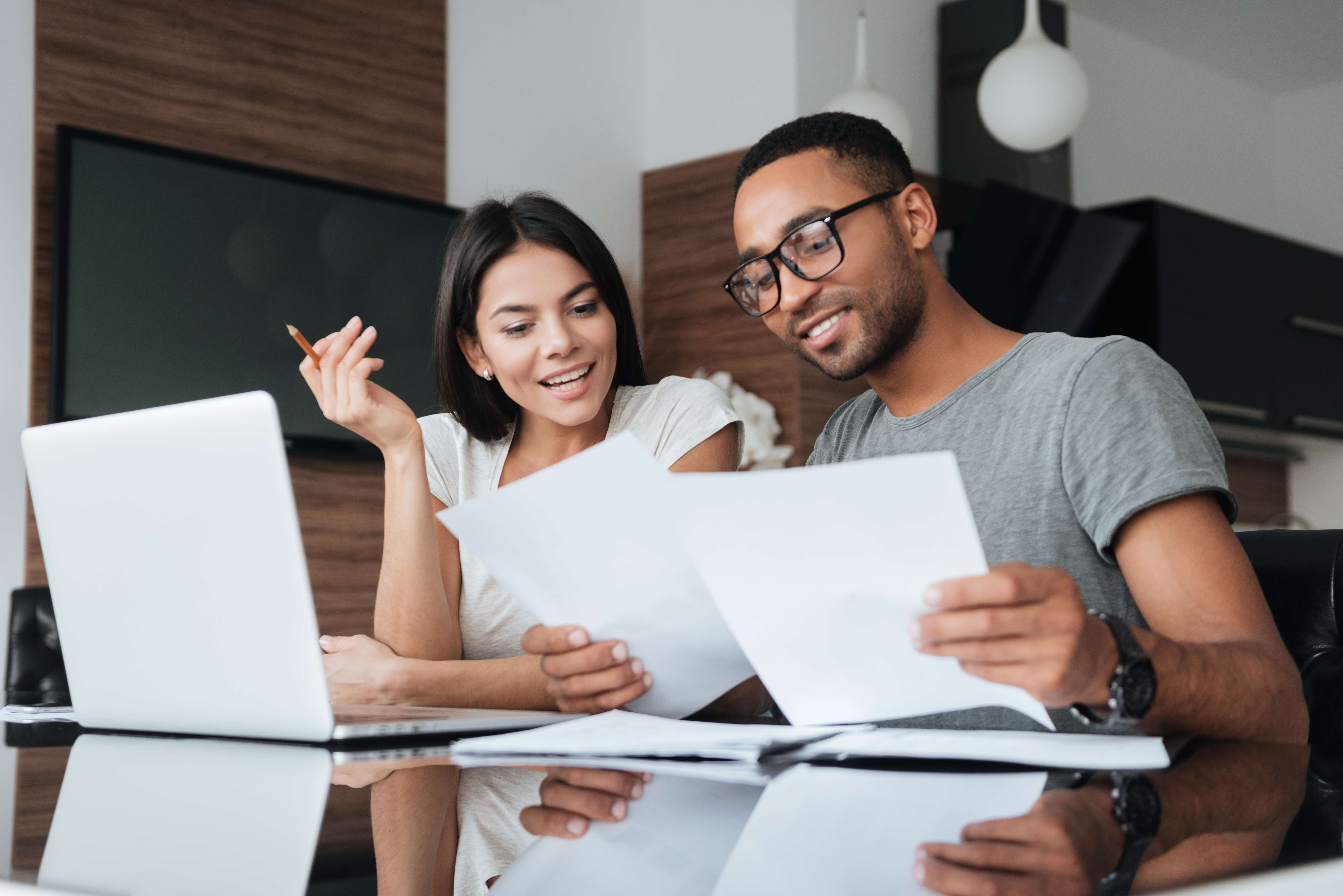 Two people sitting at a desk with a laptop and looking at sheets of paper. 